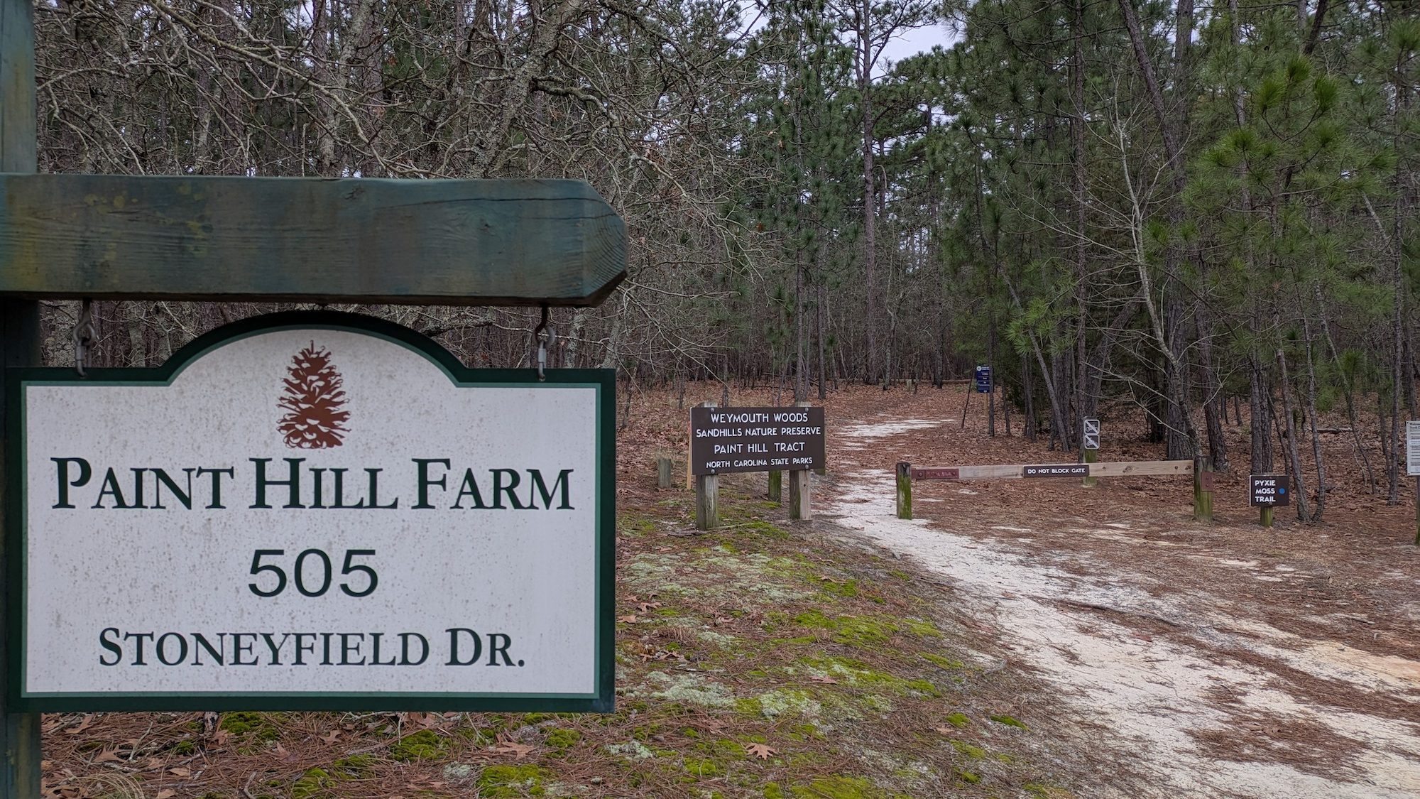 A sign reading "Paint Hill Farm" in front of a sandy driveway. 